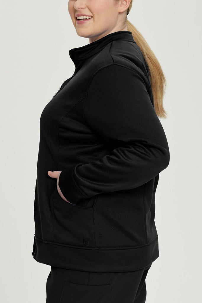 A young female Surgeon wearing an Urbane Performance Women's Zip-Up Scrub Jacket in Black size 5XL featuring stylish, princess seaming throughout.