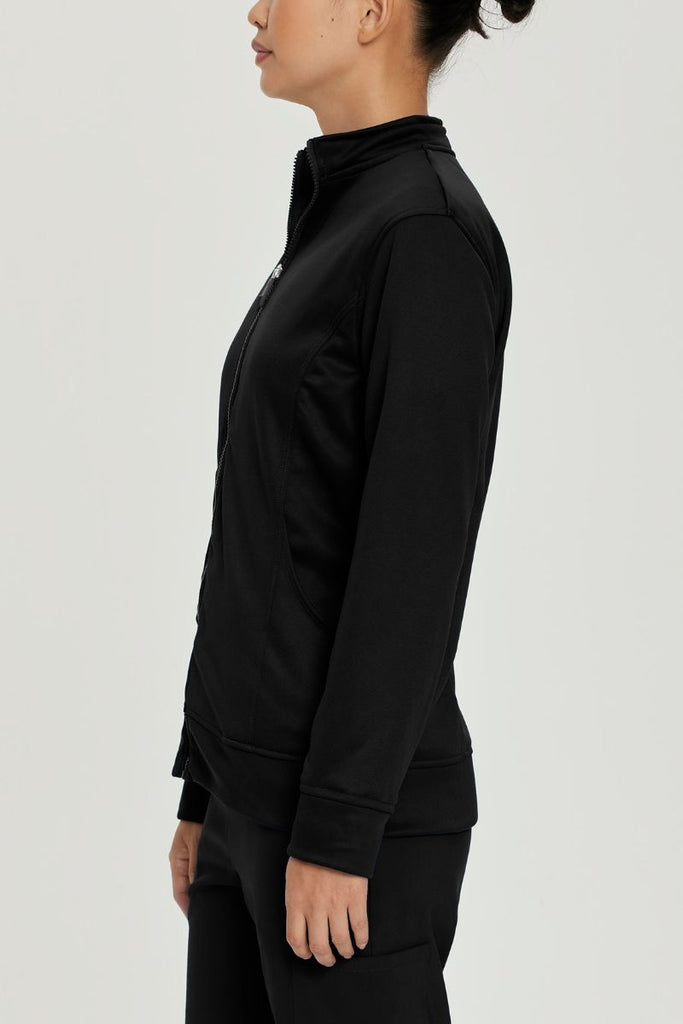 A young female Medical Assistant wearing an Urbane Performance Women's Zip-Up Scrub Jacket in Black size Large featuring moisture-wicking fabric that helps keep you dry and comfortable, even during long shifts.