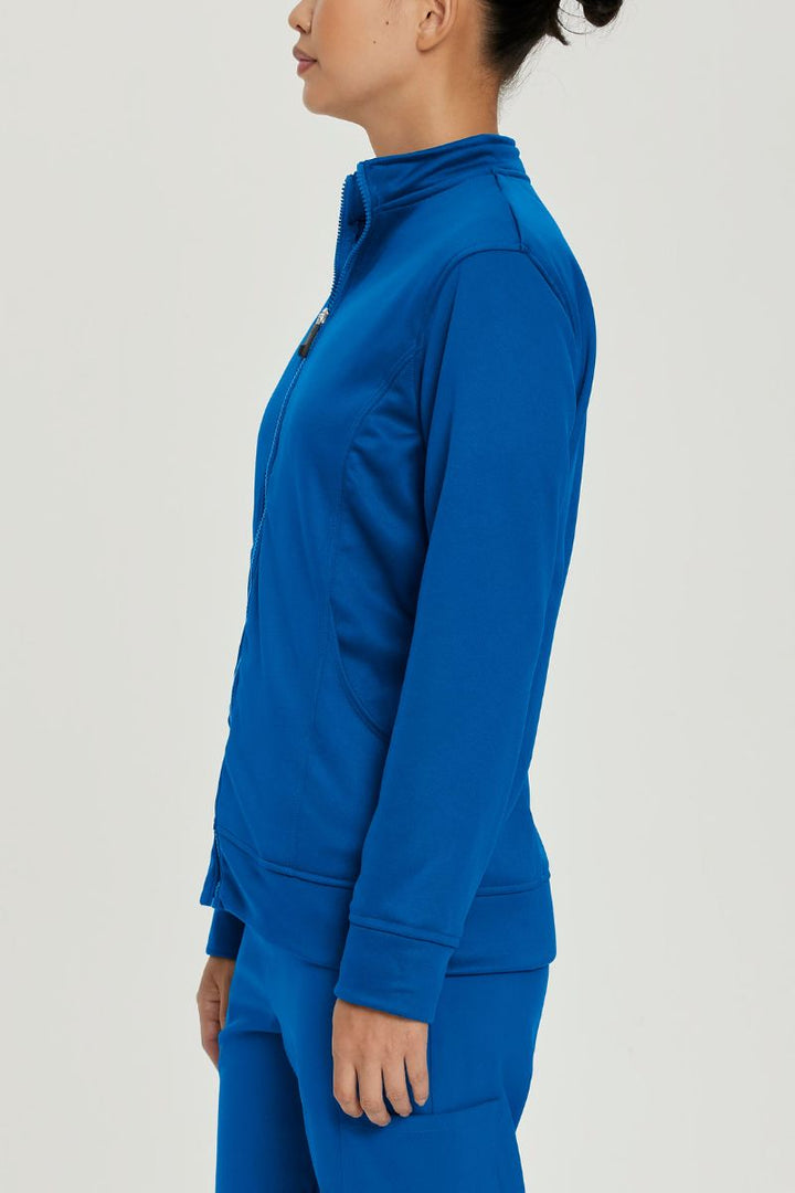 A young female Doctor wearing an Urbane Performance Women's Zip-Up Scrub Jacket in Royal Blue size Small featuring moisture-wicking fabric that helps keep you dry and comfortable, even during long shifts.