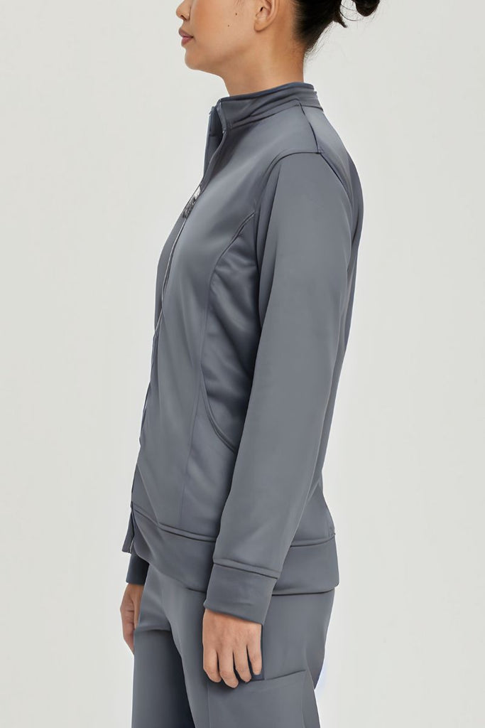 A young female Lab Tech showcasing the side of the Urbane Performance Women's Zip-Up Scrub Jacket in Steel Grey size Small featuring princess seaming throughout to provide a flattering shape.