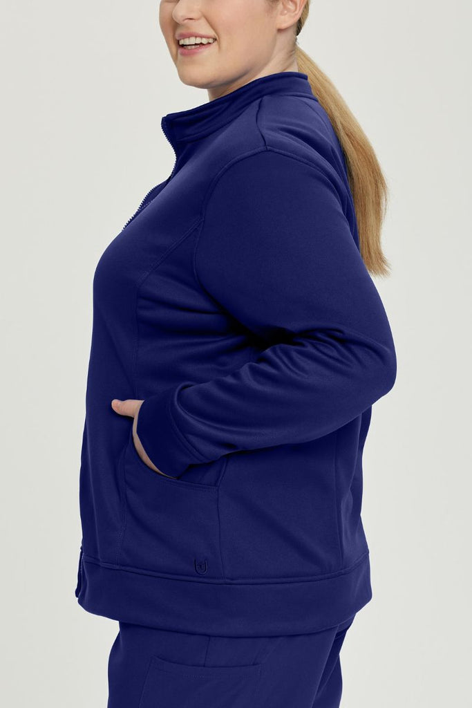A young female LPN wearing an Urbane Performance Women's Zip-Up Scrub Jacket in True Navy size 3XL featuring stylish, princess seaming throughout.