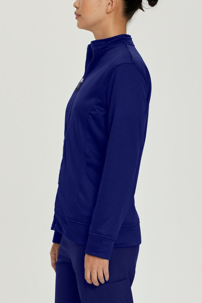 A young female Medical Assistant wearing an Urbane Performance Women's Zip-Up Scrub Jacket in True Navy size Large featuring moisture-wicking fabric that helps keep you dry and comfortable, even during long shifts.