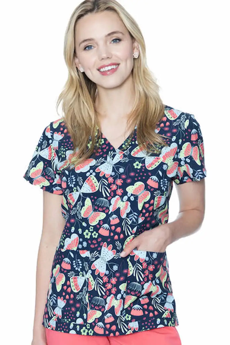 A young female Psychiatric Nurse showcasing the front of the Med Couture Women's Valerie Print Scrub Top in Butterfly Friends size large featuring a classic V-neckline and two front patch pockets.