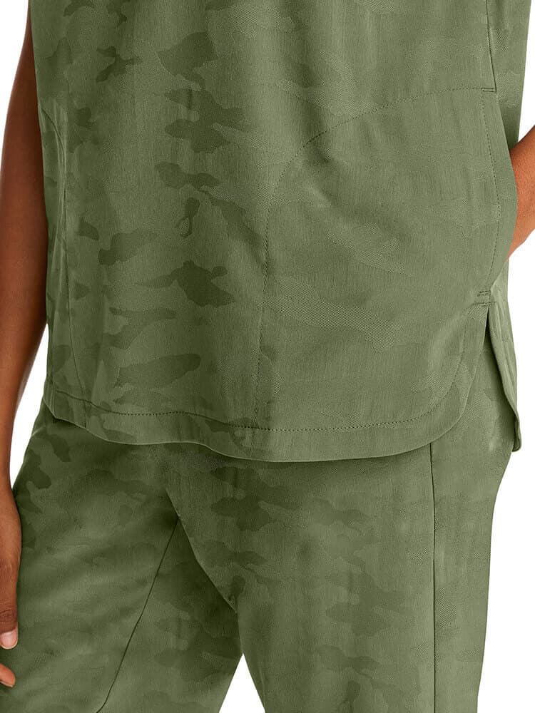 A young female Healthcare Professional wearing a Purple Label Women's Journey Camo Scrub Top in Olive size Medium featuring side slits for additional mobility.