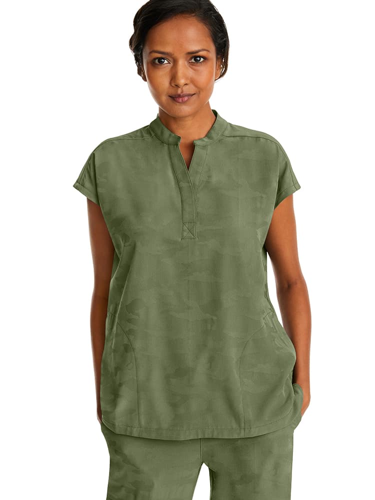 A young female Nurse Practitioner wearing a Products Purple Label Women's Journey Camo Top in Olive size Small featuring a modern fit.