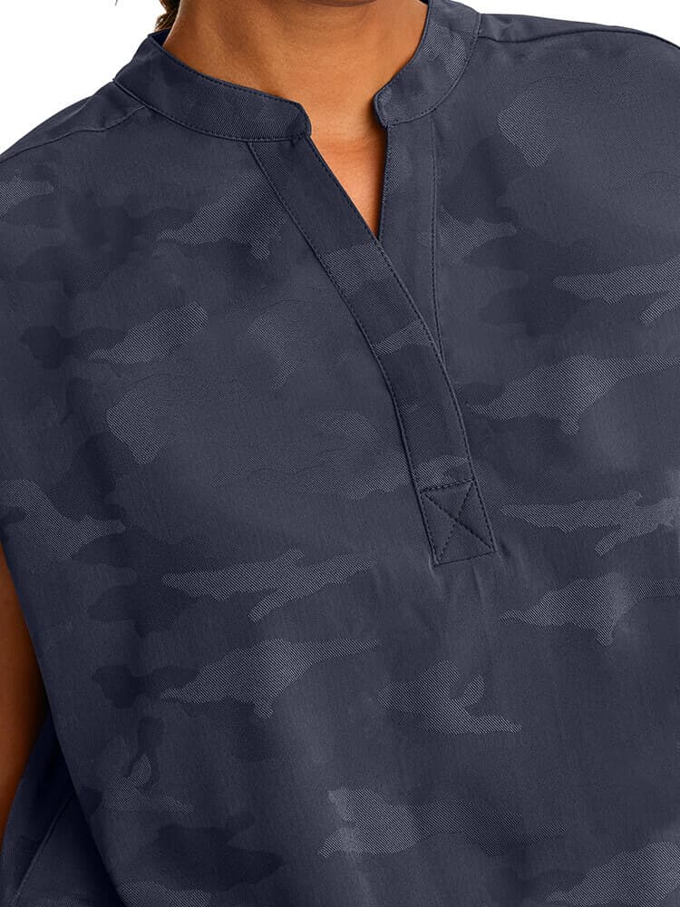 A young female Home Care Health Aide wearing a Purple Label Women's Journey Camo Top in Pewter sixe 2XL featuring a Mandarin one button collar.