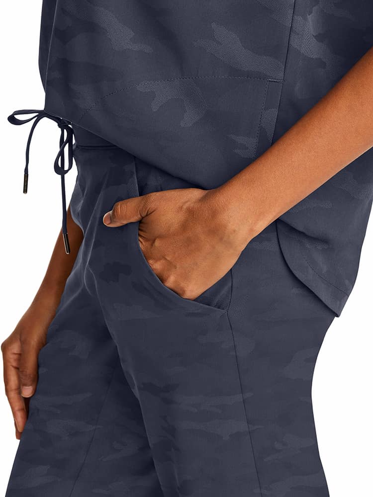 A young female Healthcare Professional wearing a Purple Label Women's Journey Camo Scrub Top in Pewter size Medium featuring side slits for additional mobility.