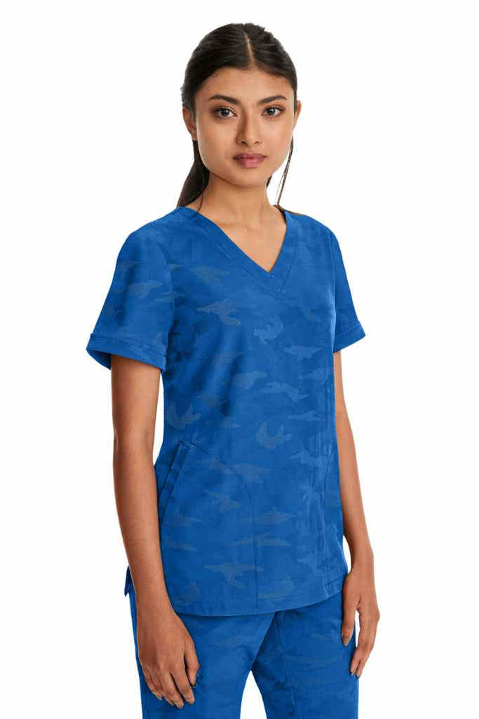 Young nurse wearing a Purple Label Women's Joy Camo Top in Royal with 2 welt pockets on each side.
