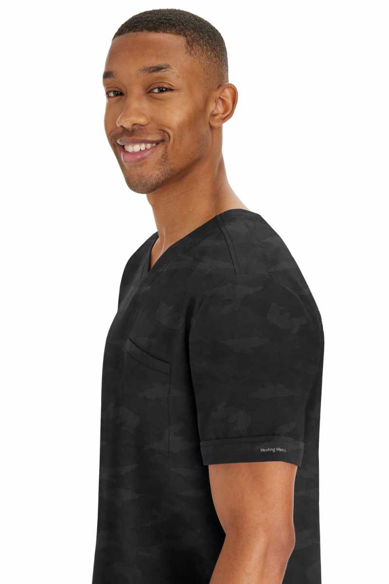 A young male physician wearing a Purple Label by Healing Hands Men's Jack Camo Top in "Black" size 2XL featuring folded cuffs at the sleeves.