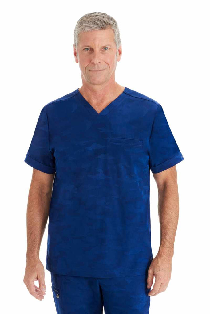 A male Nursing Assistant wearing a Purple Label by Healing Hands Men's Jack Camo Scrub Top in "Navy" size medium featuring 1 chest pocket on the wearer's left side.