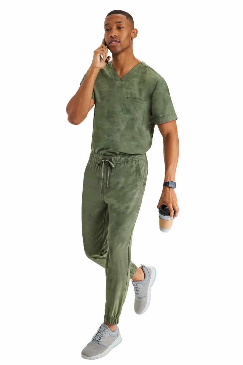 A young male Clinical Laboratory Technologist wearing a Purple Label Men's Jack Camo Scrub Top & the matching Men's Drew Camo Jogger in Olive.