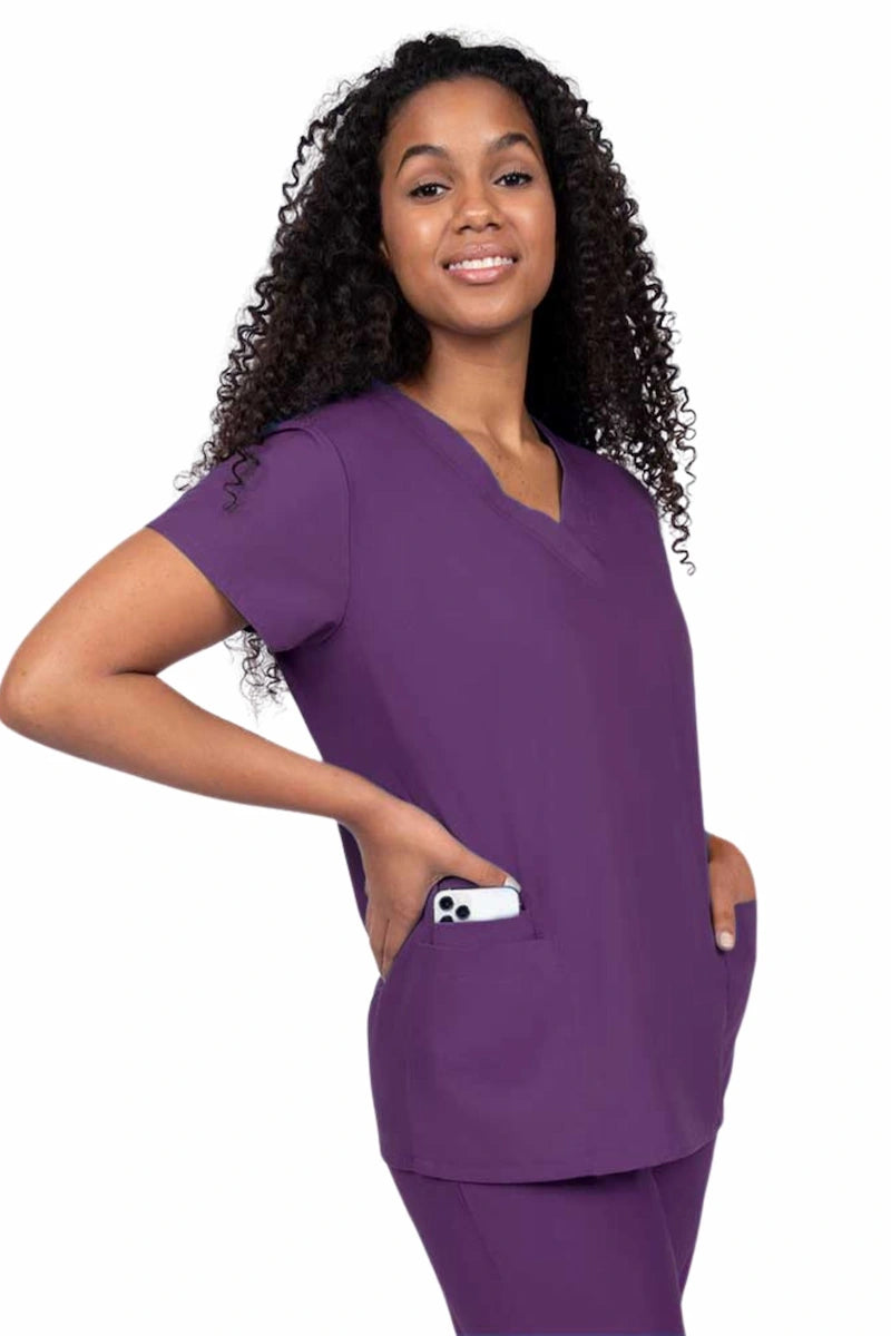 Young nurse wearing a Luv Scrubs by MedWorks Women's V-neck Scrub Top in eggplant with featuring short sleeves, and a total of 3 pockets.