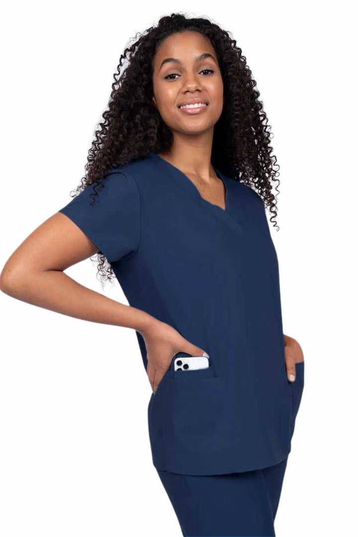 Young nurse wearing a Luv Scrubs by MedWorks Women's V-neck Scrub Top in navy with featuring short sleeves, and a total of 3 pockets.