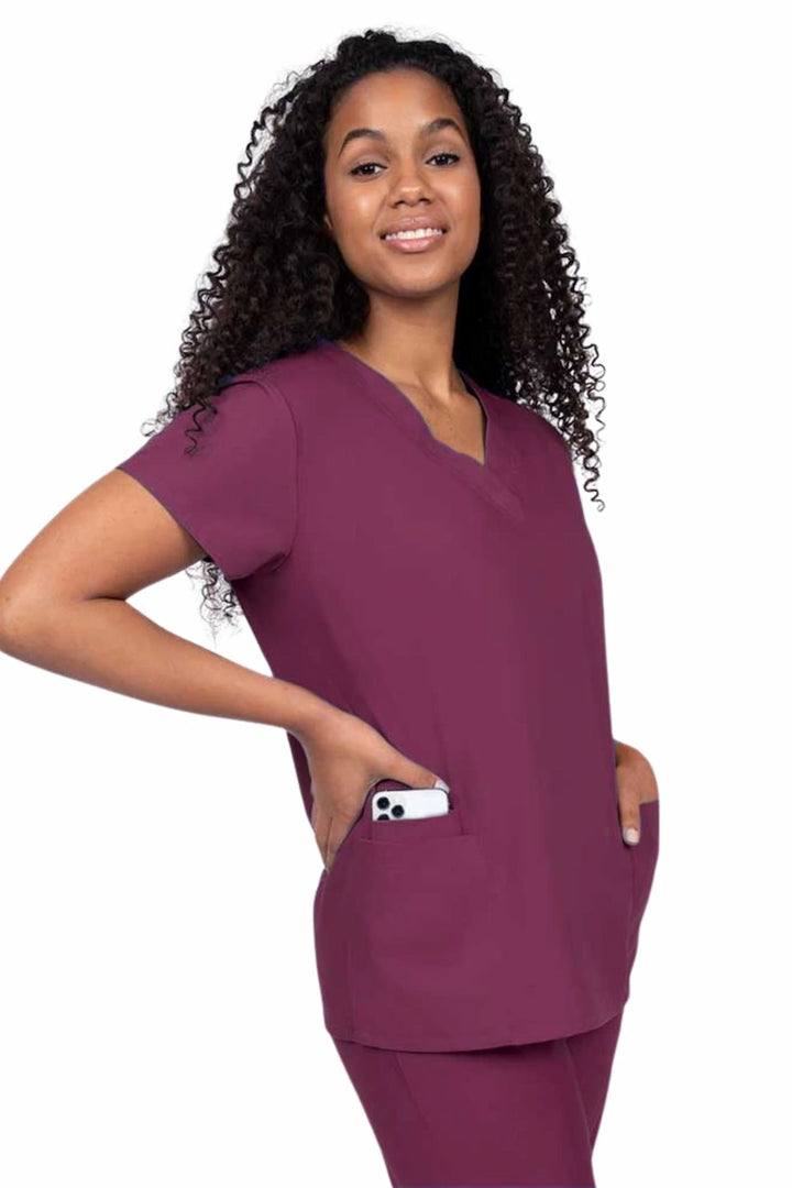 A young female surgeon wearing a Luv Scrub by MedWorks Women's V-Neck Scrub Top in Wine featuring 2 front patch pockets.