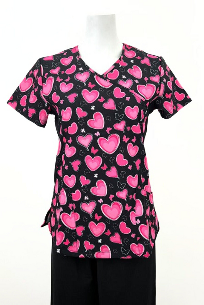 A frontward facing image of the Revel Premium Stretch Women's Mock Wrap Print Scrub Top in "Pink Hearts & Butterflies" size Medium featuring 2 front curved patch pockets &stylish seaming throughout to provide a flattering fit.