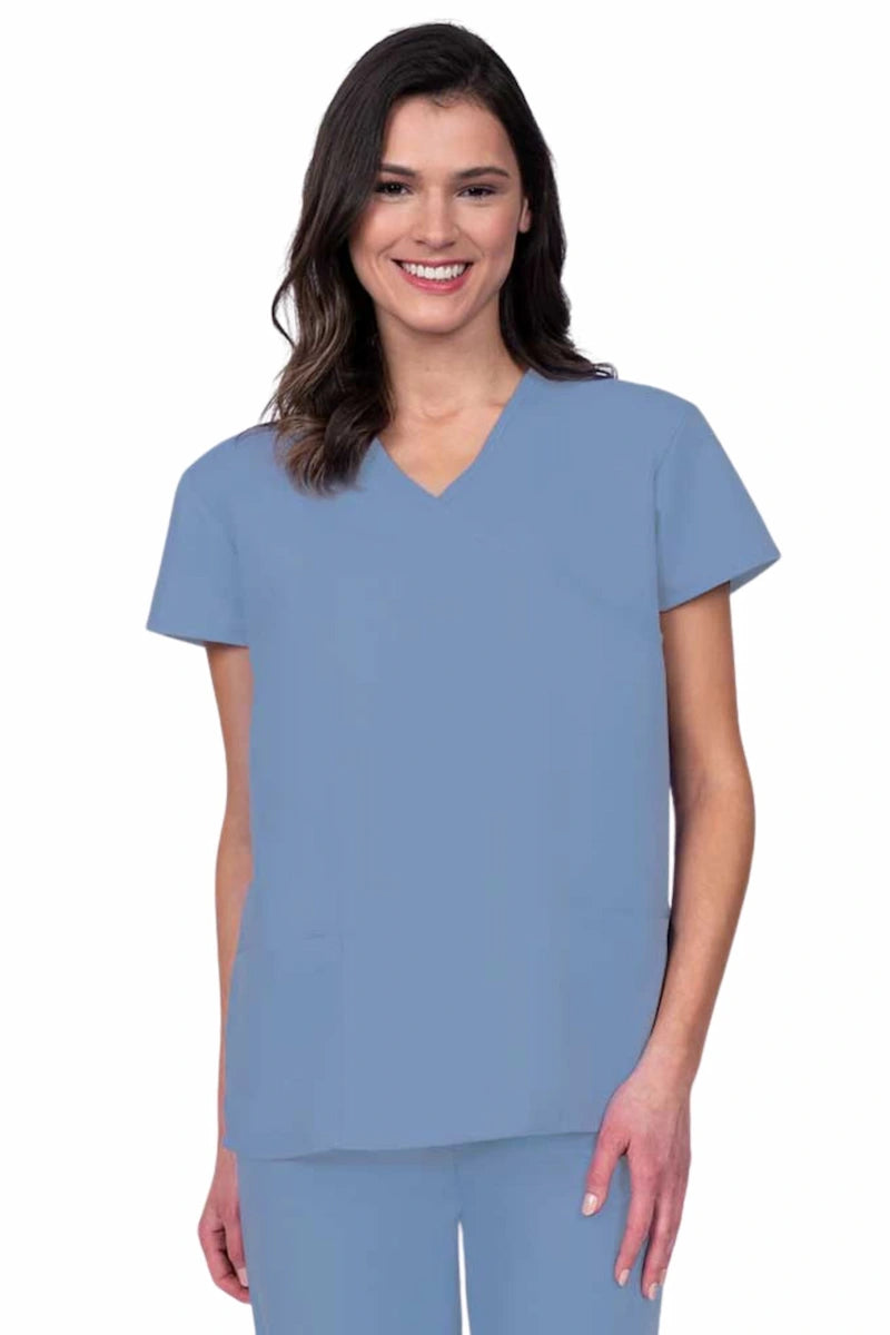 Young woman wearing a Luv Scrubs by MedWorks Women's Mock Wrap Scrub Top in ceil featuring a Y-neckline and side slits for additional range of motion.