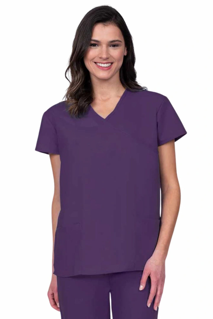 Young woman wearing a Luv Scrubs by MedWorks Women's Mock Wrap Scrub Top in eggplant featuring a Y-neckline and side slits for additional range of motion.