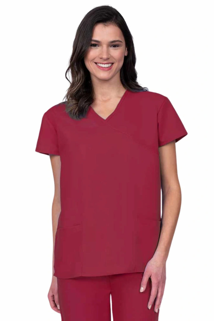 Young woman wearing a Luv Scrubs by MedWorks Women's Mock Wrap Scrub Top in red featuring a Y-neckline and side slits for additional range of motion.