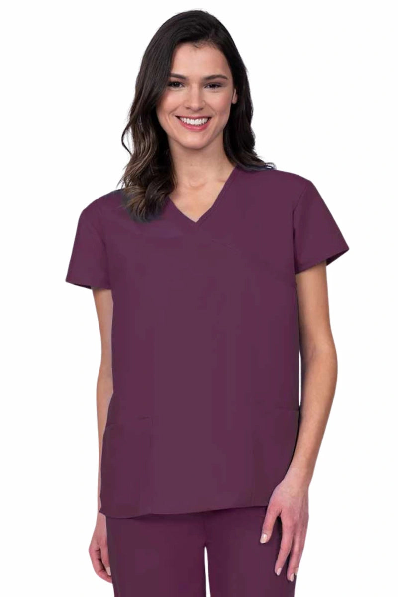 Young woman wearing a Luv Scrubs by MedWorks Women's Mock Wrap Scrub Top in wine featuring a Y-neckline and side slits for additional range of motion.