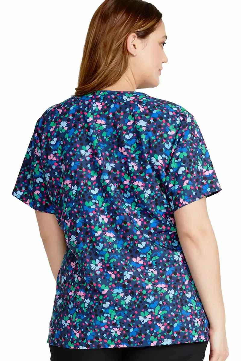 A yougn female Nurse showcasing the back of the Cherokee Women's Mock Wrap Printed Scrub Top in Confetti Daisies featuring a center back length of 26".