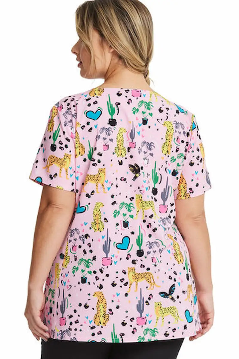 A young female Psychiatric Nurse showcasing the back of the HeartSoul Women's V-Neck Printed Scrub Top in Jungle of Love featuring a center back length of 26".