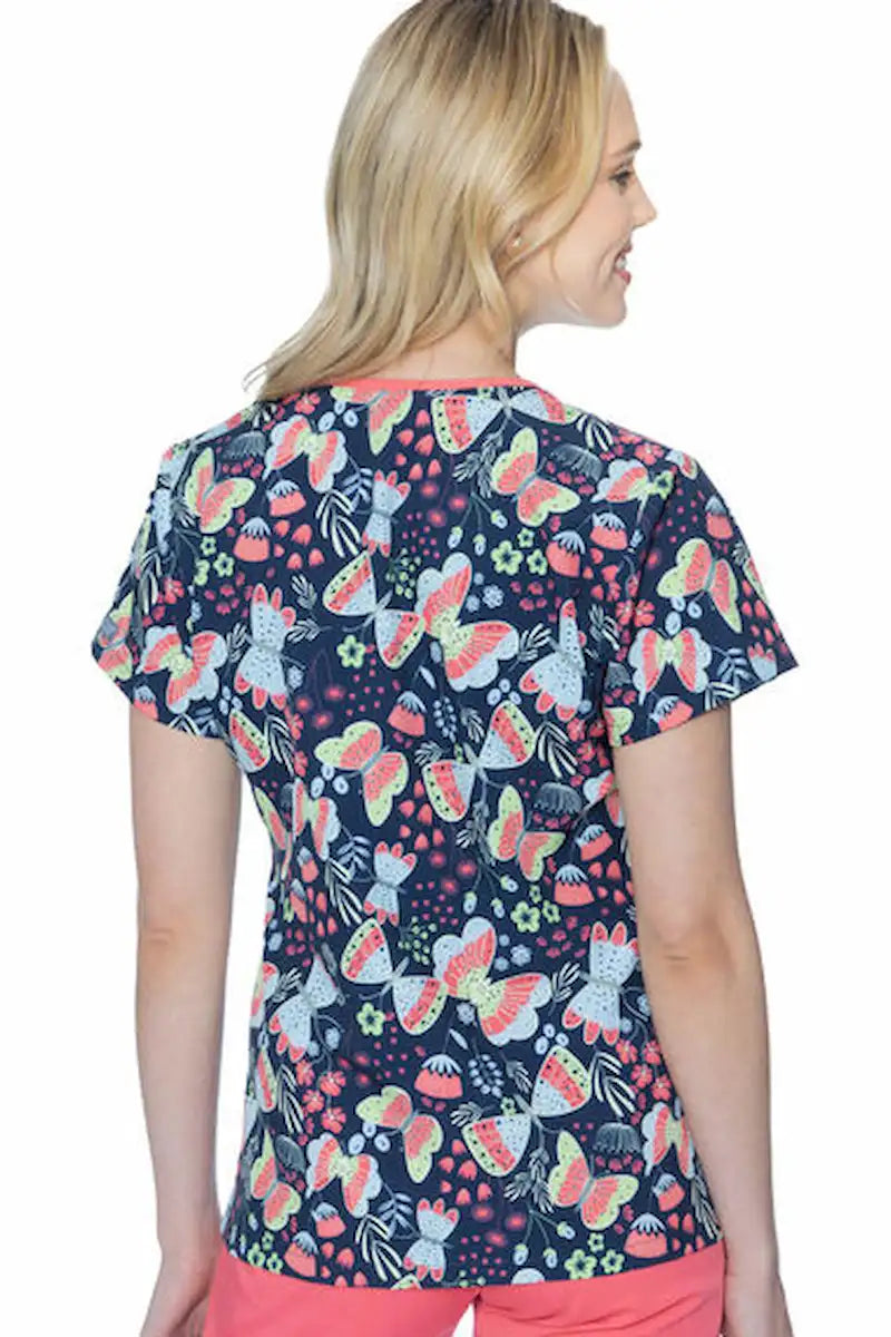 A young female Pediatric Nurse showcasing the back the Med Couture Women's Valerie Printed Scrub Top in Butterfly Friends featuring a center back length of 26.5".