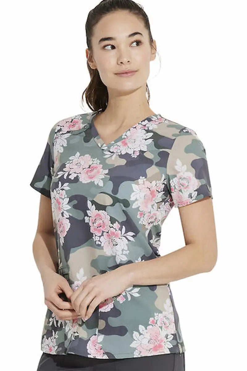 A young female Children's Nurse wearing a Dickies Women's V-Neck Print Scrub Top in "Camo's Abloom" featuring a contemporary fit and short sleeves.