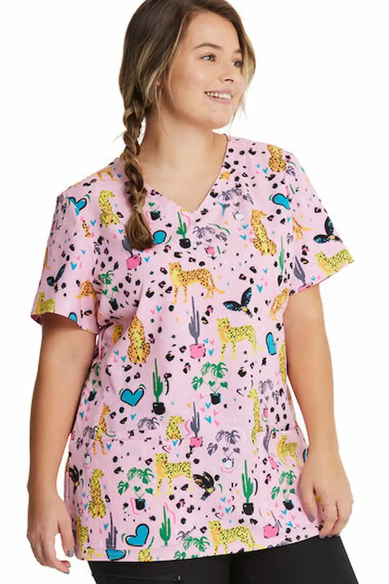 A young female children's nurse wearing a HeartSoul Women's V-Neck Print Scrub Top in Jungle of Love featuring a shaped V-neckline.