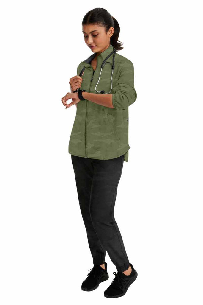 A young female Nurse Practitioner wearing a Purple Label Women's Destini Camo Scrub Jacket in Olive size 2XL featuring a stand collar.