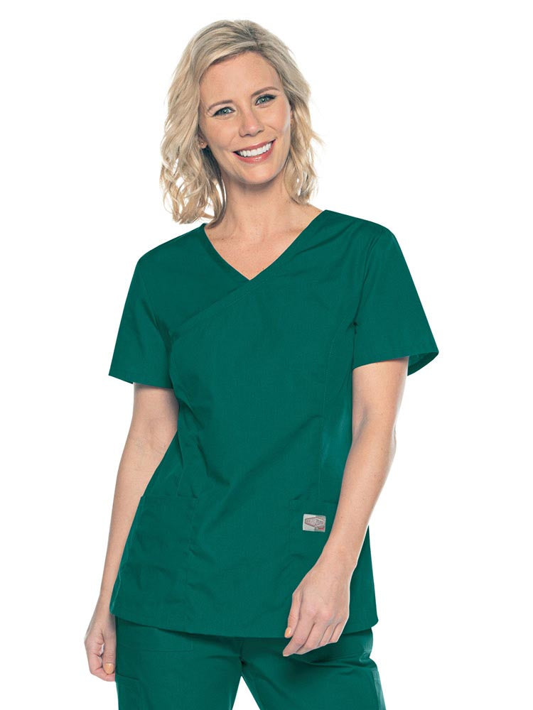 A young female Medical Assistant wearing a Landau ScrubZone Women's Mock Wrap Top in Hunter size Small featuring a modern tailored fit.
