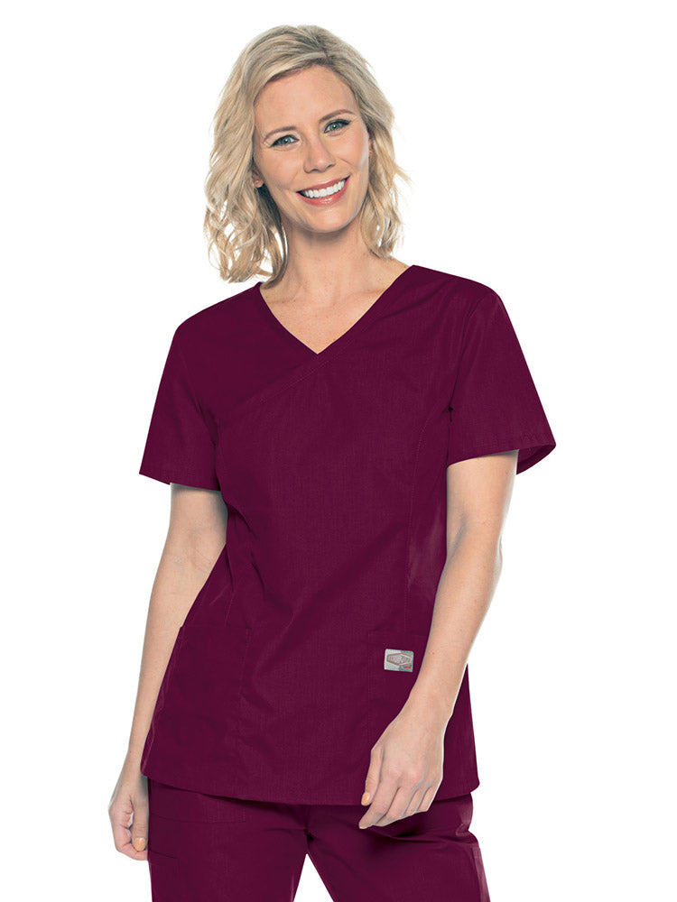 A young female Medical Assistant wearing a Landau ScrubZone Women's Mock Wrap Top in Wine size Small featuring a modern tailored fit.