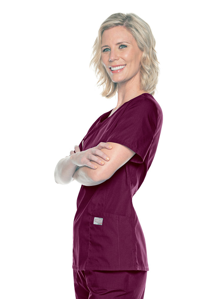 A young female Nursing Assistant wearing a Landau Women's Mock Wrap Scrub Top in Wine size Medium featuring short sleeves.