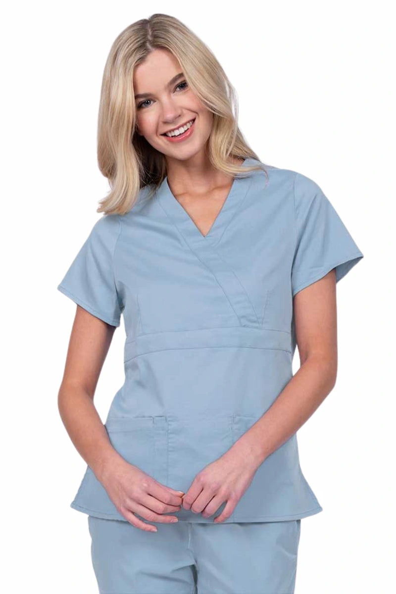 Young woman wearing an Epic by MedWorks Women's Mock Wrap Scrub Top in blue fog with a unique fabric content of 77% Polyester, 21% Viscose, 2% Spandex.