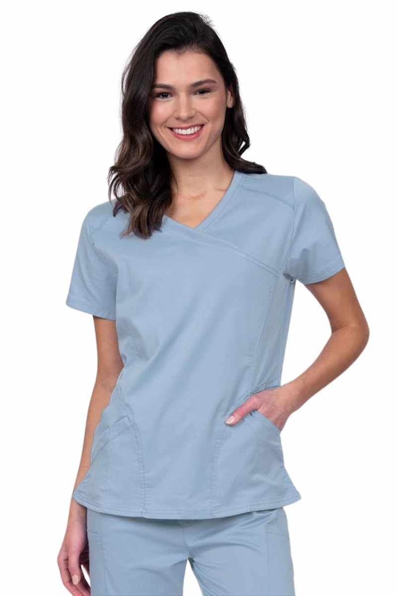 Young RN wearing an Epic by MedWorks Women's Knit Collar Mock Wrap Scrub Top in blue fog featuring a Y-neckline with short sleeves.