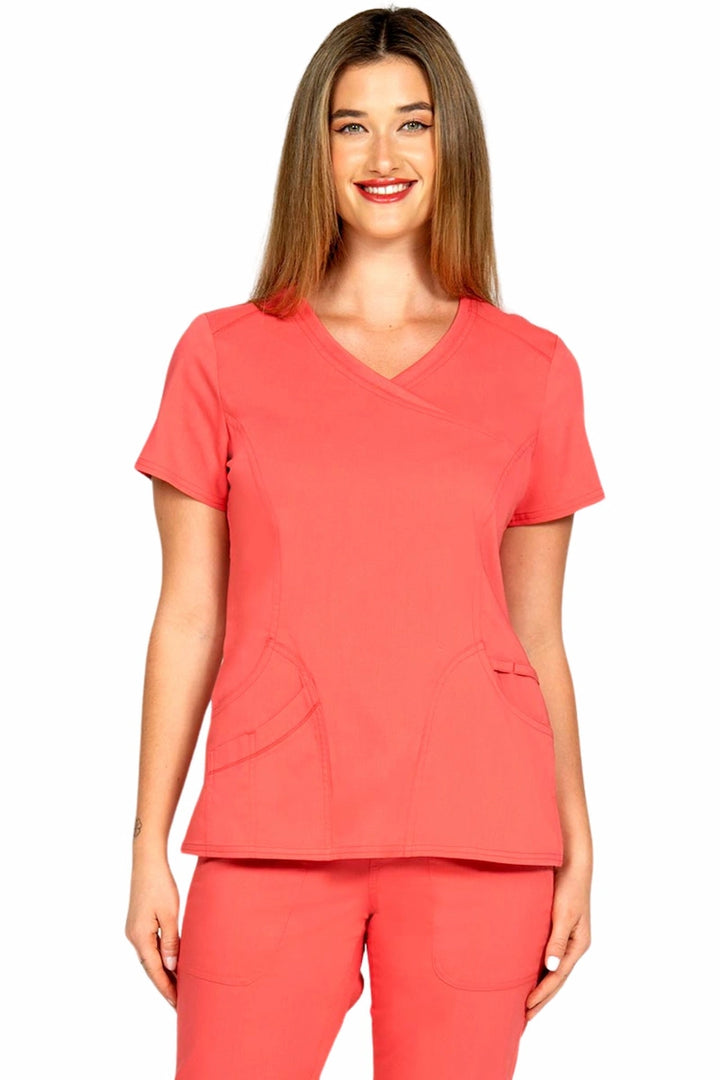 A young female Phlebotomist wearing an Epic by MedWorks Women's Knit Collar Mock Wrap Scrub Top in Coral size small featuring a y-neckline & short sleeves.