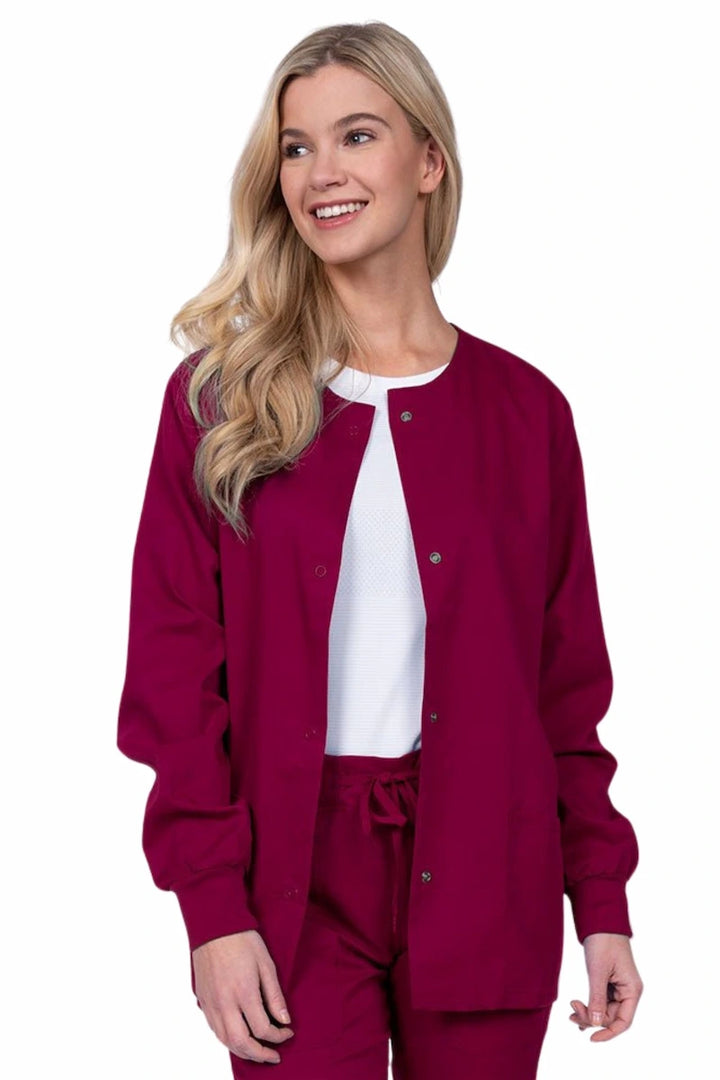 Young female healthcare worker wearing an Epic by MedWorks Women's Snap Front Scrub Jacket in wine with two front patch pockets.