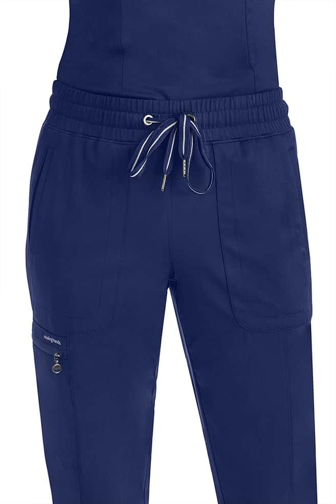 A female Nurse Practitioner wearing a Purple Label Women's Aspen Jogger Scrub Pant in "Navy" size 2XL featuring an elastic waist & an adjustable comfort drawstring.