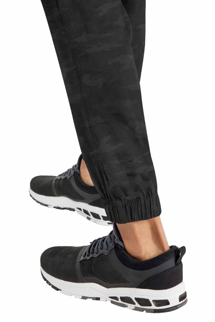 A young male Physical Therapist Aide wearing a Purple Label by Healing Hands Men's Drew Camo Jogger in Black size XL featuring elastic cuffs at the leg opening.