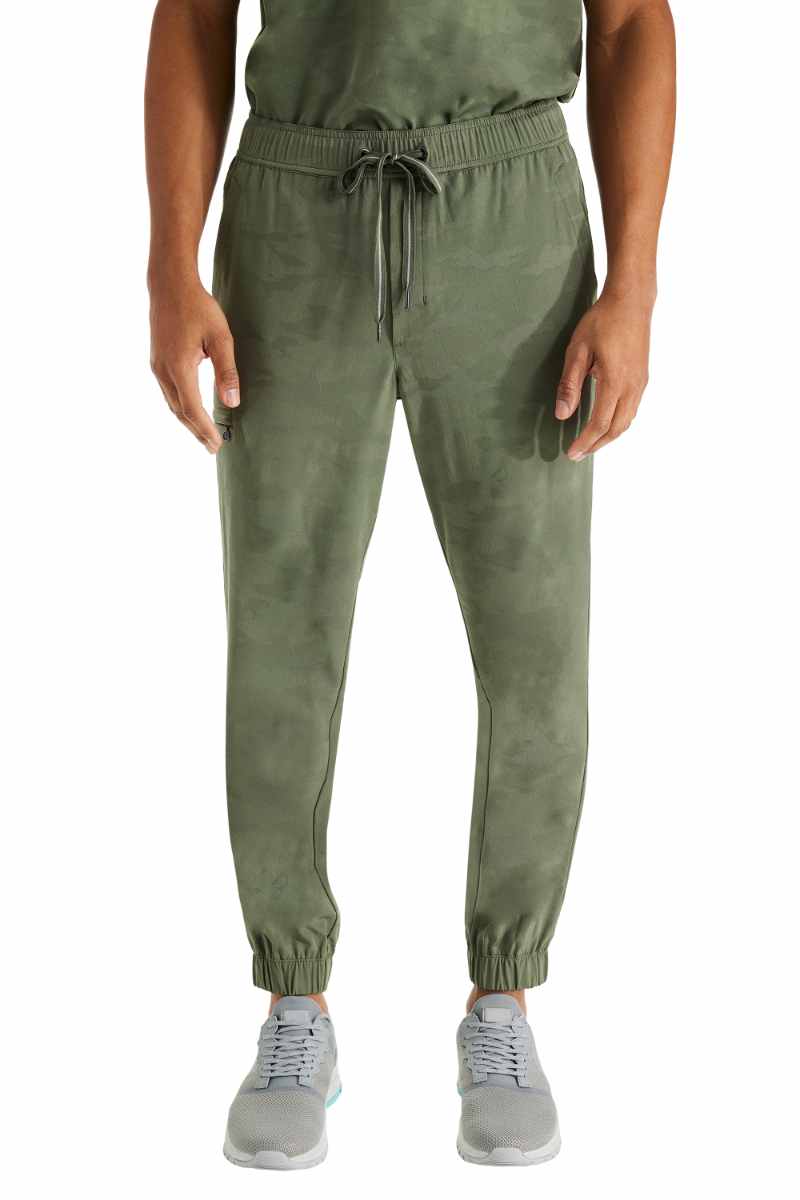 A young male Physician Assistant wearing a pair of Men's Drew Camo Joggers from Purple Label by Healing Hands in Olive size Medium.