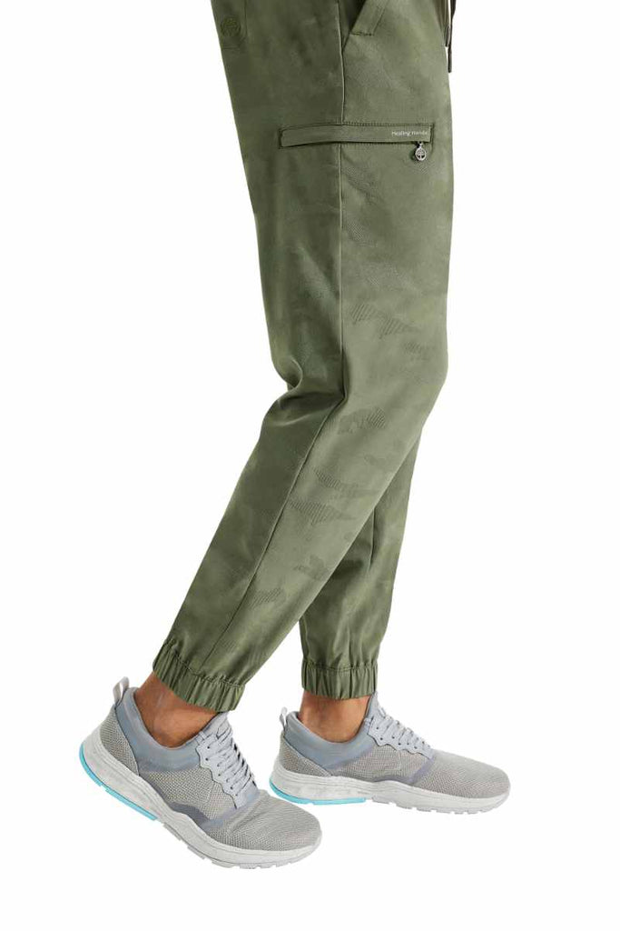 A young male Physical Therapist Aide wearing a Purple Label by Healing Hands Men's Drew Camo Jogger in Olive size XL featuring elastic cuffs at the leg opening.