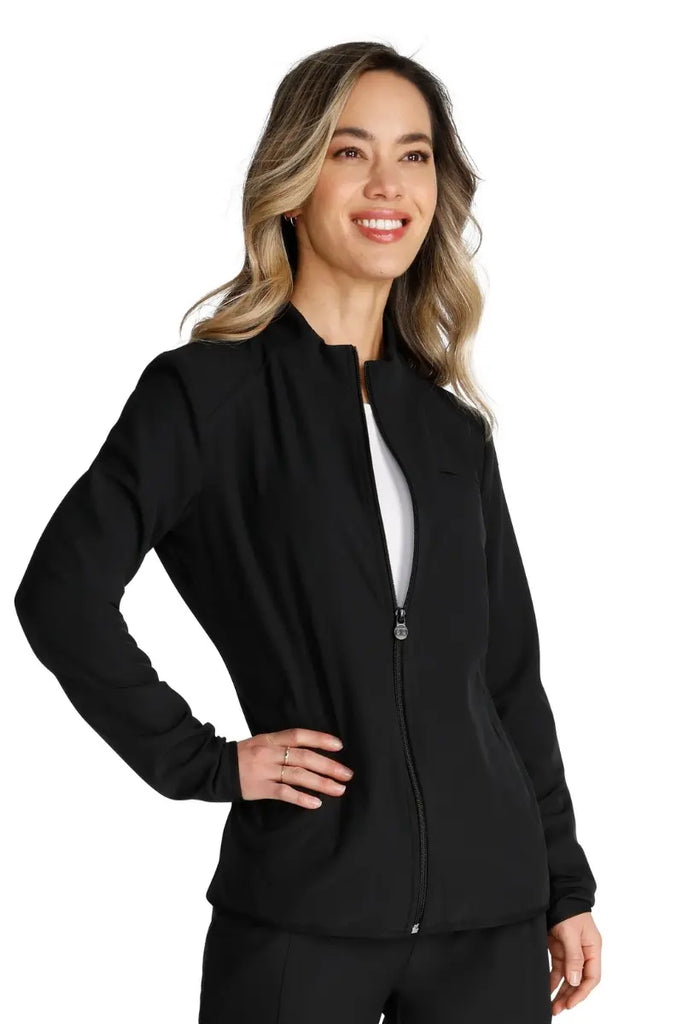 A young Medical Assistant wearing an Allura Women's Zip-Up Scrub Jacket in Black featuring a full length zip front closure.
