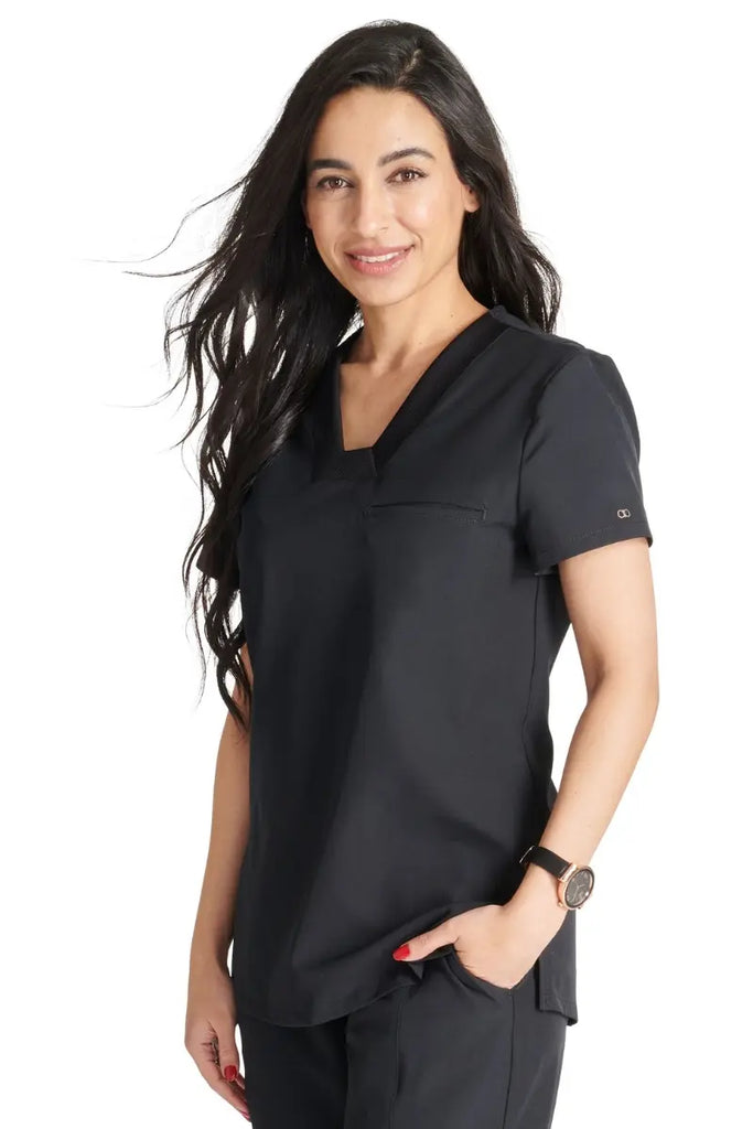 A female LVN wearing an Allura Women's Mitered Scrub Top in Black featuring side vents.