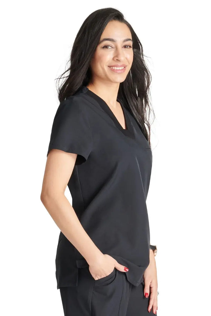 A young female EMT wearing an Allura Women's Mitered V-Neck Scrub Top in Black size Medium featuring a single welt chest pocket on the left side.