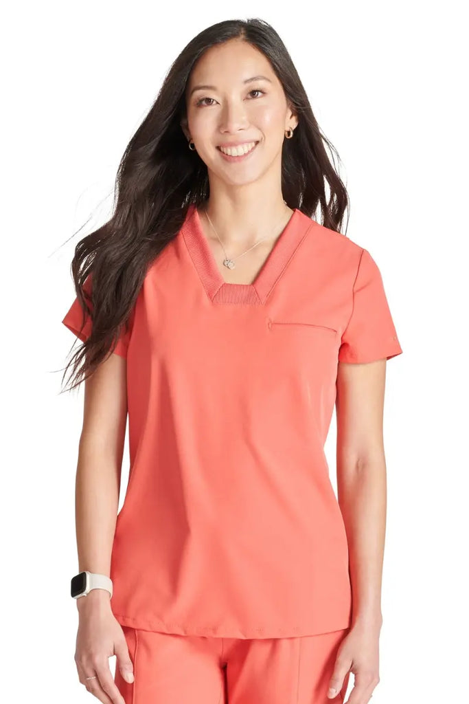 A young female Maternity Nurse wearing an Allura Women's Mitered V-neck Scrub Top in Cayenne size Small.