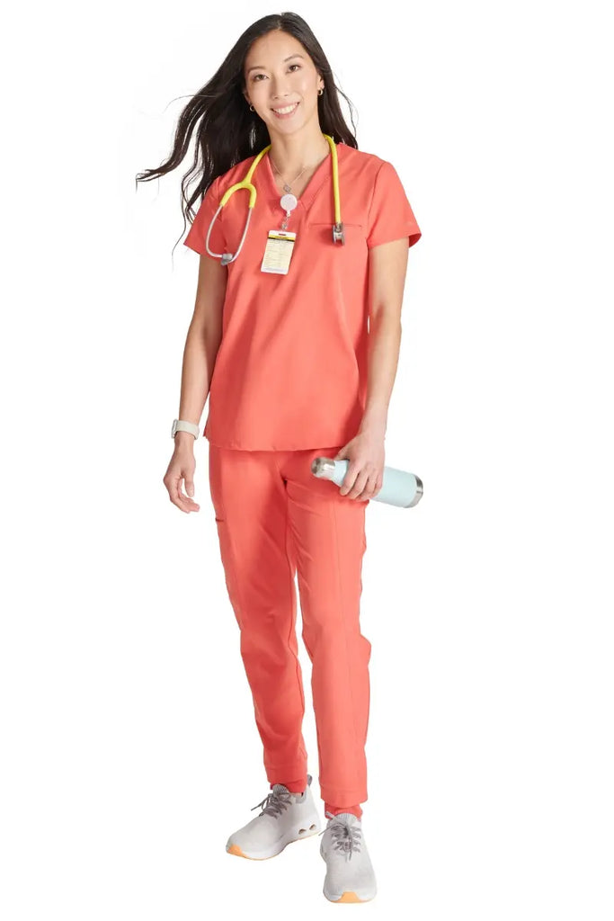 A full body shot of a young female Labor and Delivery Nurse wearing an Allura Women's scrub uniform in Cayenne size Large.