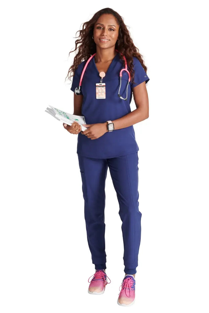 A full body shot of a young female nurse wearing an Allura Women's scrub uniform in Navy Blue size small.