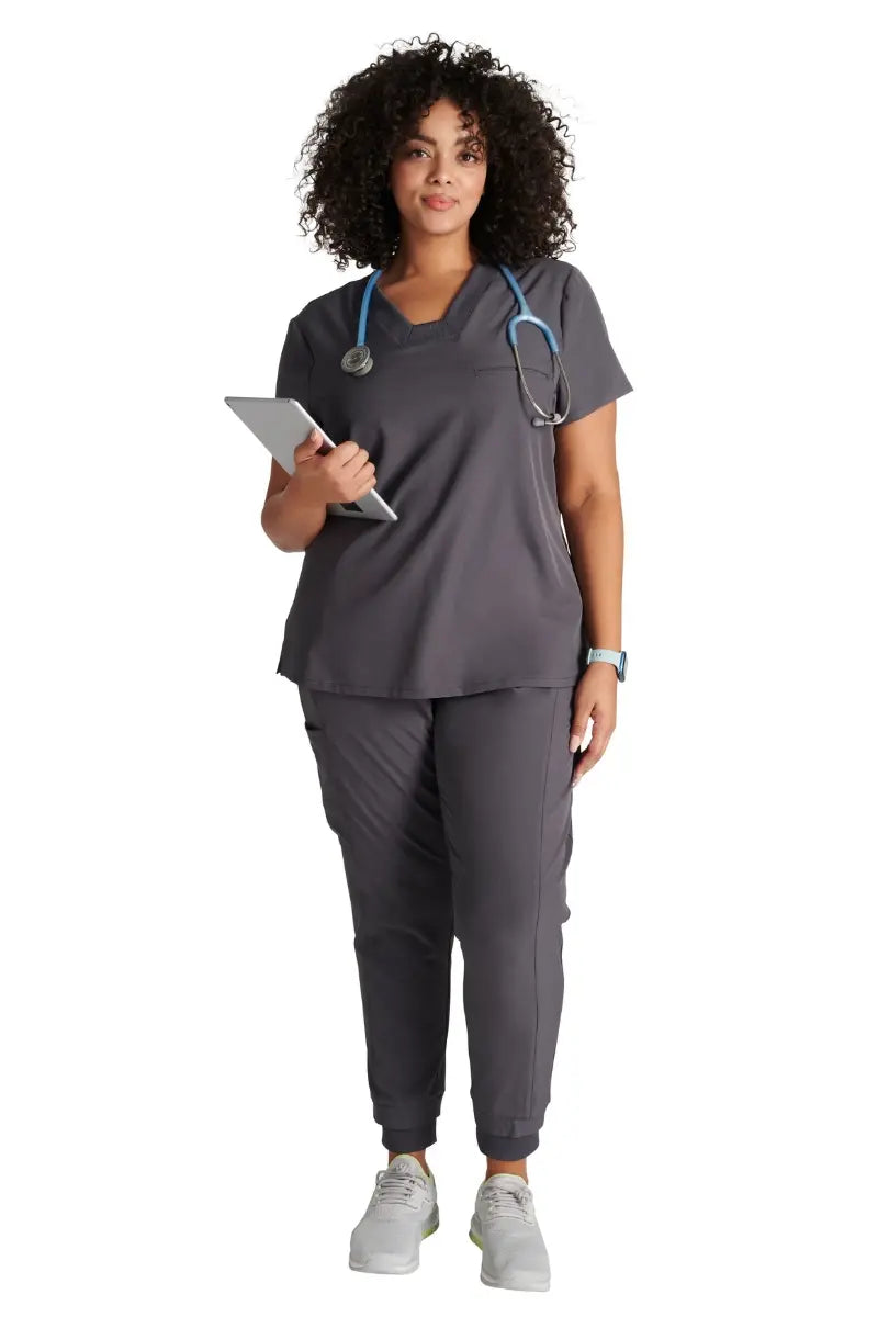 A full body shot of a young female LVN wearing an Allura Women's scrub uniform in Pewter size 2XL.