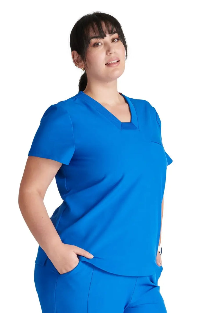 A female CNA wearing an Allura Women's Mitered Scrub Top in Royal Blue featuring side vents.