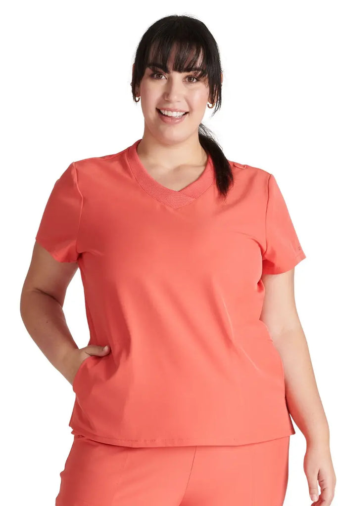 A young female Home Health Aide wearing the Allura Women's Stylized V-neck Scrub Top in Cayenne size 2XL.