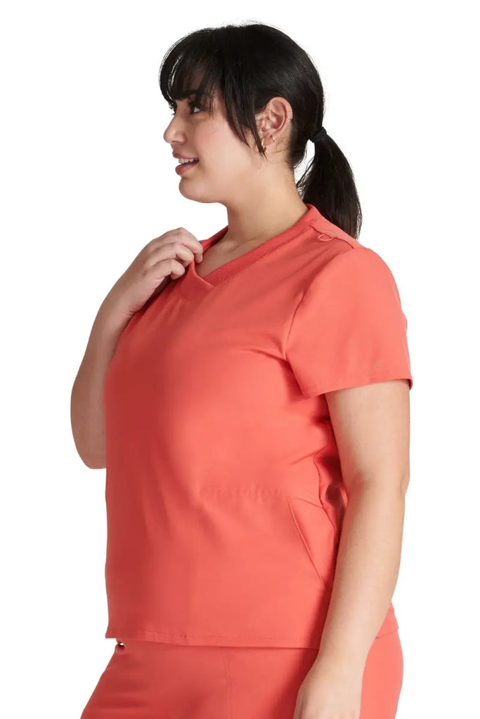 A female Medical Assistant wearing an Allura Women's Stylized V-neck Scrub Top in Cayenne featuring a contemporary fit.